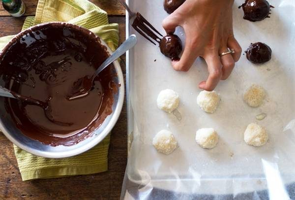 Dark chocolate in a mixing bowl and dipping in coconut bites.