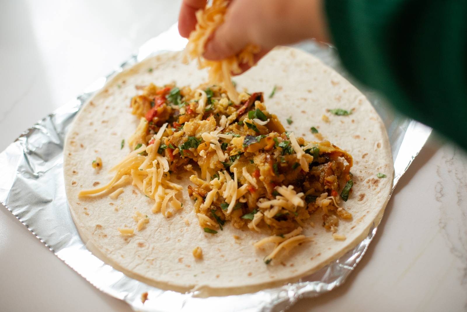 Sprinkling cheese on a breakfast burrito.