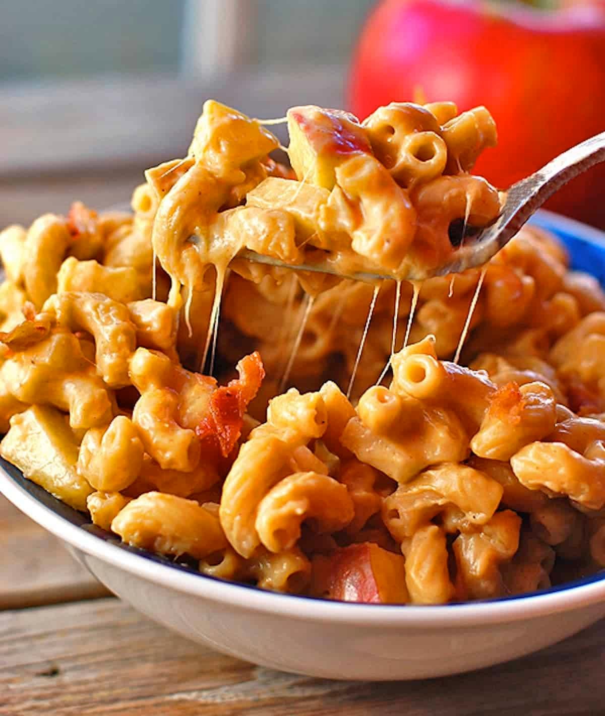 Butternut squash mac and cheese with caramelized onions, crispy bacon, and fresh sweet apples on a fork.
